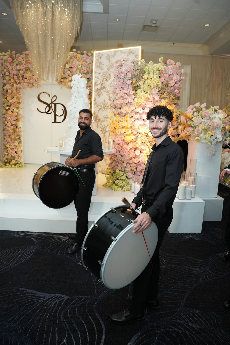 Two Prestige Brothers drummers before a floral wall and wedding cake